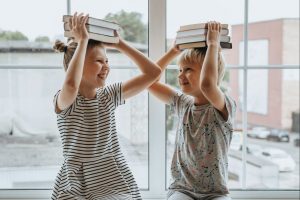 Deux enfants souriants portent des livres sur leur tête