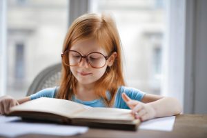 Une petite fille rousse avec des lunettes lit un livre